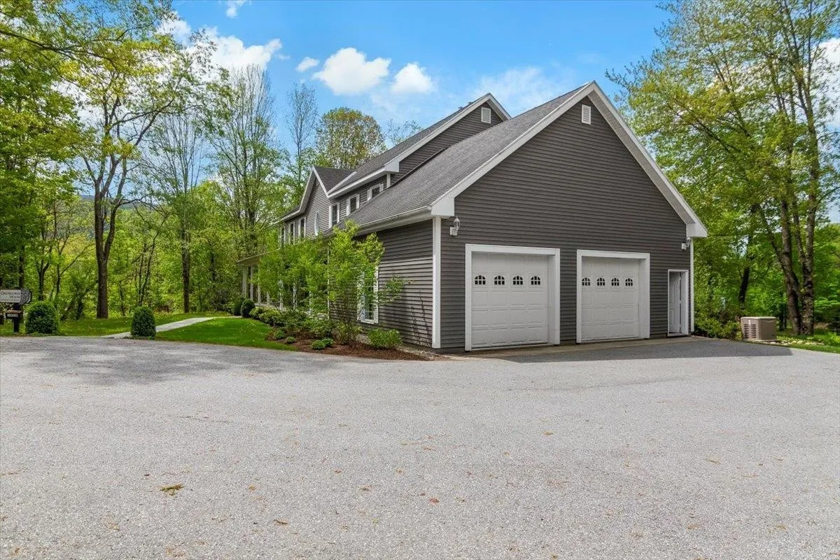 A large gray house with three garage doors surrounded by trees.